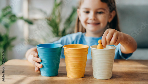 The girl learns colors by playing with wooden cylindrical toy colored human figures and placing them in cups of the appropriate color. The child is happy that he completed the task photo