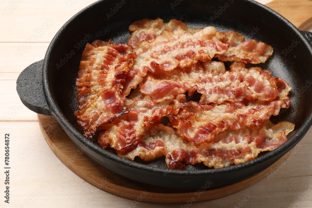 Delicious bacon slices in frying pan on white wooden table, closeup