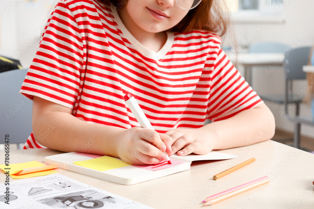 Cropped photo of red head schoolgirl writing in notebook while sitting at the desk in classroom Cropped photo of red head schoolgirl writing in notebook while sitting at the desk in classroom