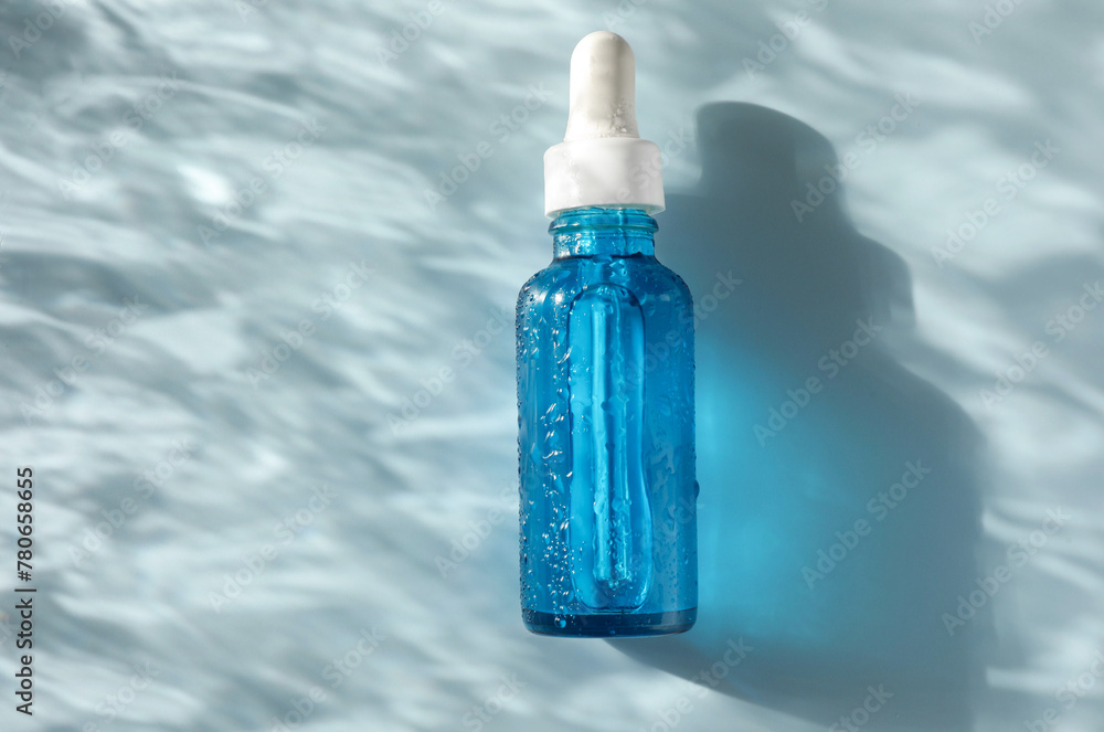 Wet bottle of cosmetic serum on light blue background, top view. Space for text Wet bottle of cosmetic serum on light blue background, top view. Space for text