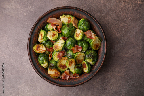 Delicious roasted Brussels sprouts and bacon in bowl on brown table, top view