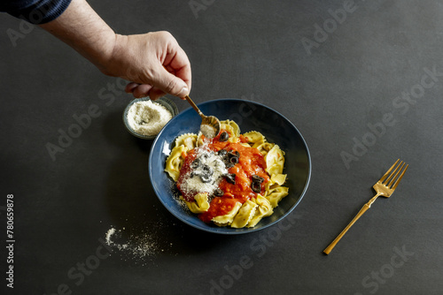 Photographing a man's hand sprinkling grated cheese on Italian pasta with tomato on a black surface second model