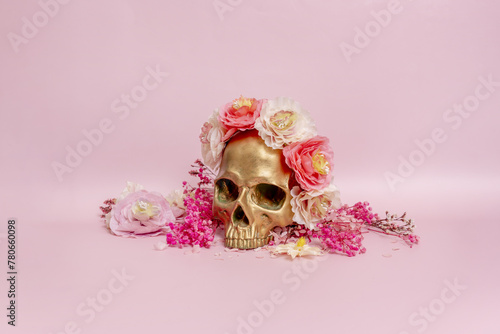 Fototapeta Naklejka Na Ścianę i Meble -  A golden skull surrounded by dried flowers on a soft pink surface posing for photo