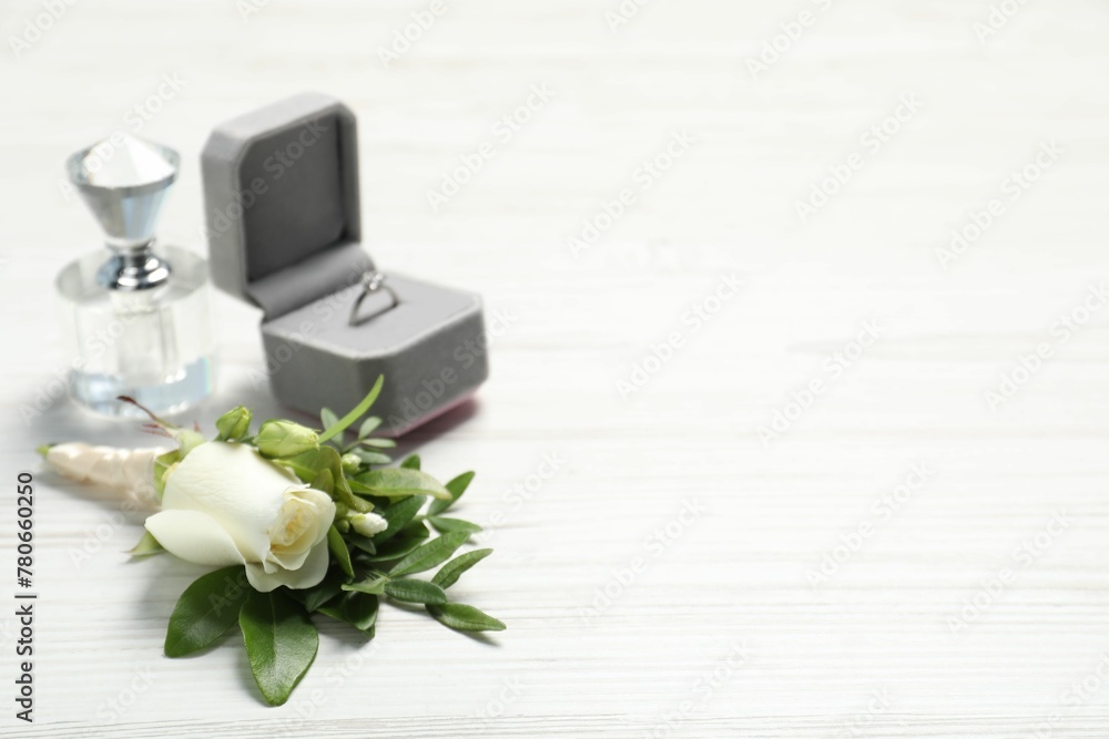 Wedding stuff. Stylish boutonniere, perfume and ring on white wooden table, closeup. Space for text