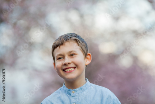 Cute smiling boy walks along the street of cherry blossoms. Happy children. Warm bright spring.
