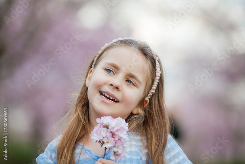 Cute smiling girl is walking along the street of cherry blossoms. Happy children. Warm bright spring.