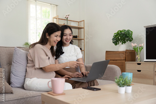 Senior mother and adult daughter relaxing and looking at laptop together at home © Natee Meepian