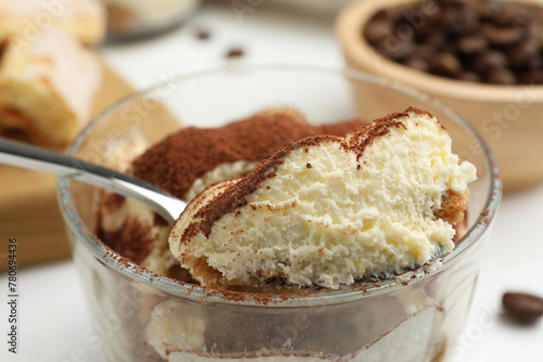 Delicious tiramisu in glass and spoon on table, closeup