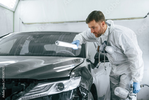 Front part of the automobile. Garage worker is holding lighting and checking surface of the car