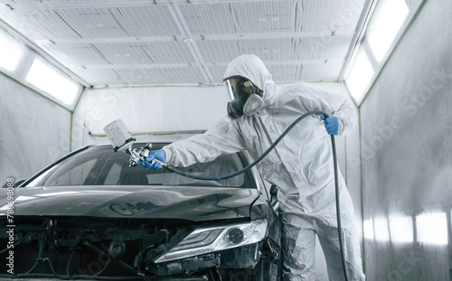 White protective wear. Man is painting a car by using spray guy © standret
