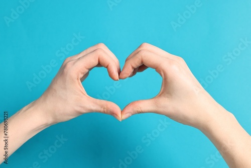 Woman showing heart gesture with hands on light blue background  closeup