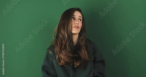 Brunette woman looking by side with sad expression over isolated green background. Break up and divorce, difficult period of life. Mental health. Girl wear green pullover. photo