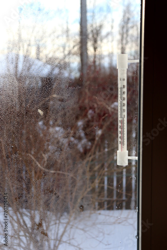 A plastic retro thermometer outside the window of a village house on a frosty day. View from the window into the courtyard, vertical photo