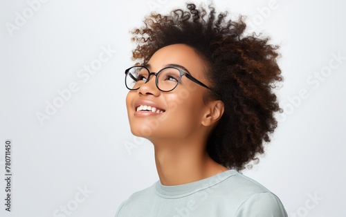 Young woman with curly hair and glasses looking up with a joyful expression  on a light background