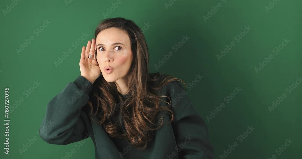 Cute curious woman keeps hand near ear tries to overhear something very interesting listens somebody secret looks camera likes collecting rumors poses against green background. Eavesdropping concept. Cute curious woman keeps hand near ear tries to overhear something very interesting listens somebody secret looks camera likes collecting rumors poses against green background. Eavesdropping concept.