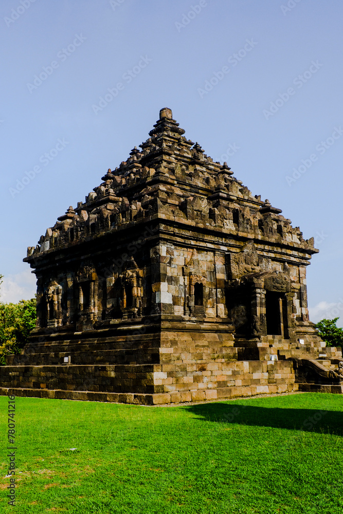 A large stone temple with a pyramidal roof, surrounded by lush green grass. The temple appears to be an ancient Hindu or Buddhist structure with architectural details. A large stone temple with a pyramidal roof, surrounded by lush green grass. The temple appears to be an ancient Hindu or Buddhist structure with architectural details.
