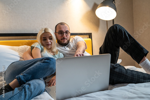 Young couple is engrossed in content on laptop, man and woman entertainment or collaboration, while relaxing in bed.