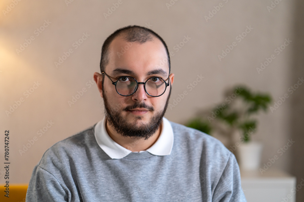 Fototapeta premium Portrait of focused young man with glasses, looking at camera, in well-lit indoor setting. 