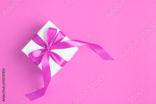 Gift box with tied pink bow on the pink background. Top view. Copy space.
