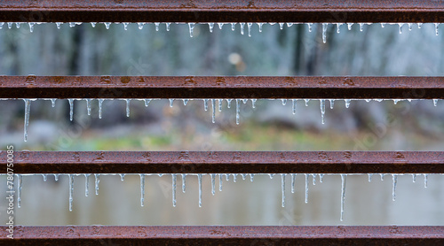 Horizontal, rusted, iron bars in fence covered in thick ice from a winter storm.  Featuring good symmetry and perfectly level horizontal lines.