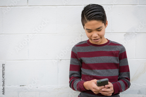 Happy, smiling teenage asian boy with braces having fun using his smartphone