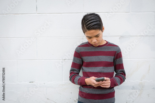 Fashionable teenage asian boy standing alone against a white background using his smartphone.