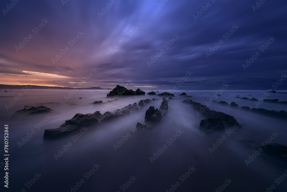 Obraz premium Flysch of Barrika beach, Bizkaia, at sunset with a dramatic sky of warm colors and the tide water entering between the rocks