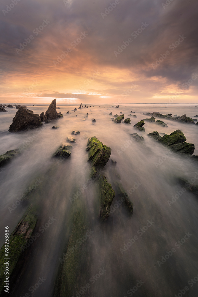 Flysch of Barrika beach, Bizkaia, at sunset with a dramatic sky of warm colors and the tide water entering between the rocks