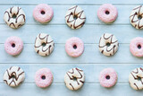 Flatlay of frosted vanilla donuts with chocolate swilrs and strawberry pink doughnuts with coconut flakes. Overhead table top view. Flatlay background.