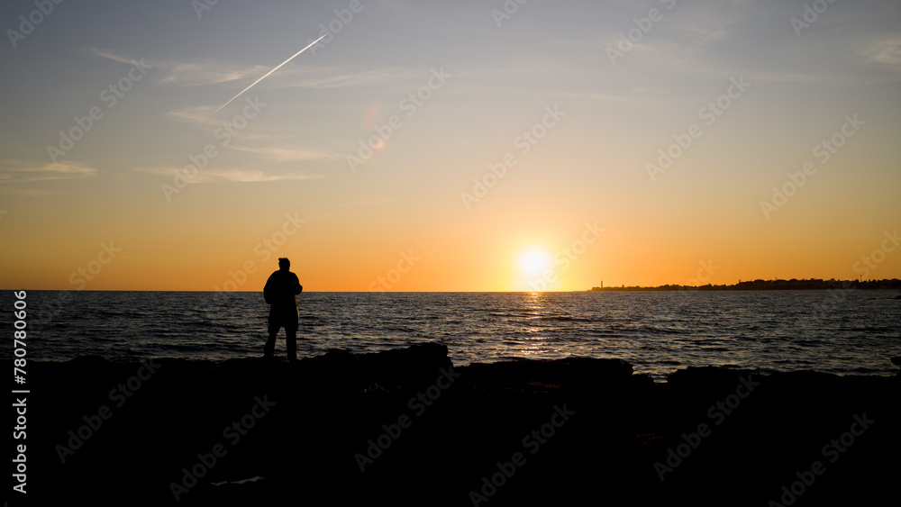 Ragazzo gurda il tramonto dagli scogli a Marina di Ragusa