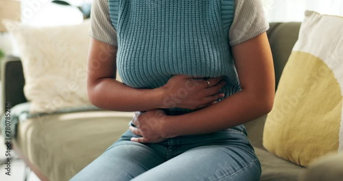 Woman, stomach ache and sick pain in home for menstruation, digestion or inflammation. Person, hands and bloated abdomen on sofa for uterus cramps with discomfort for tummy virus, ulcer or gut health photo