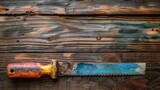Top view of a saw with a colorful handle against a rustic wooden backdrop