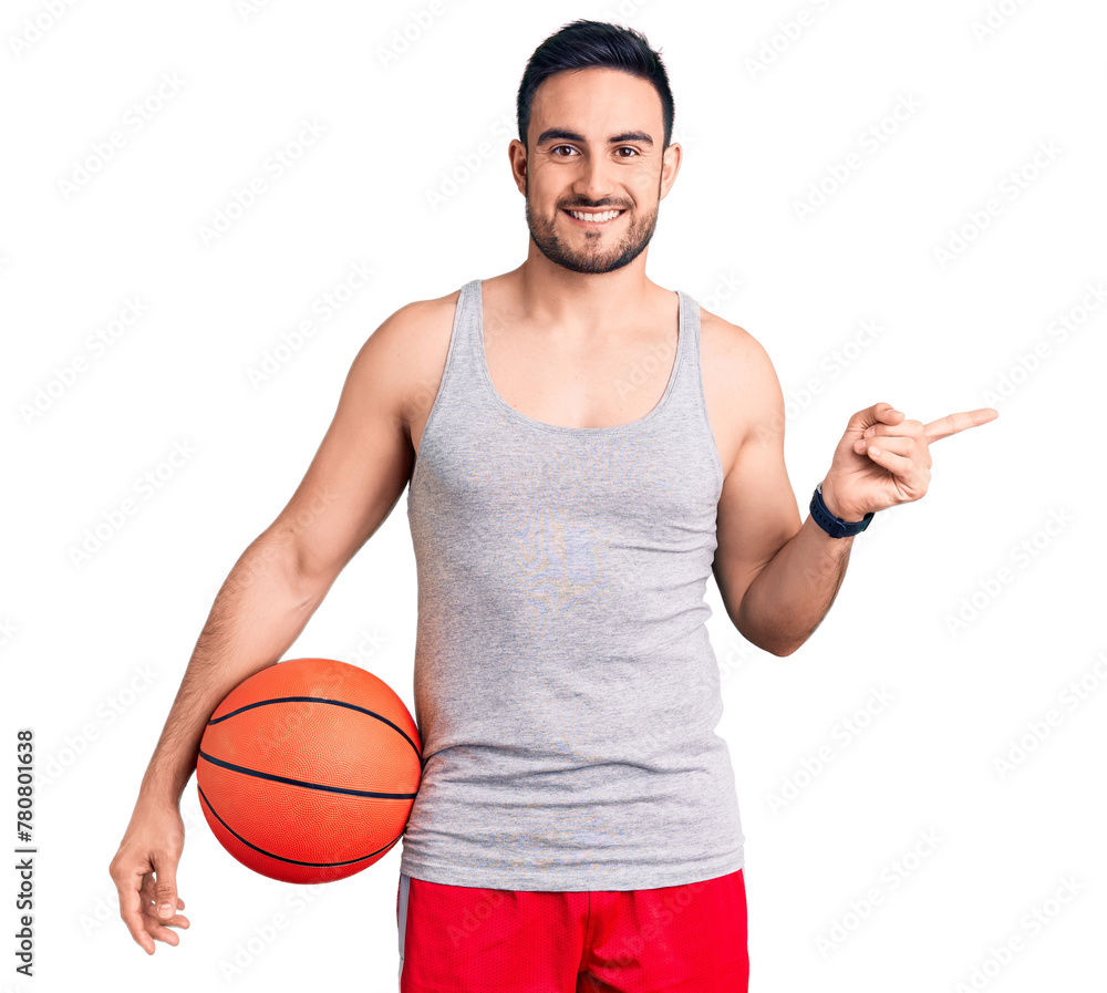 Young handsome man holding basketball ball smiling happy pointing with hand and finger to the side Young handsome man holding basketball ball smiling happy pointing with hand and finger to the side