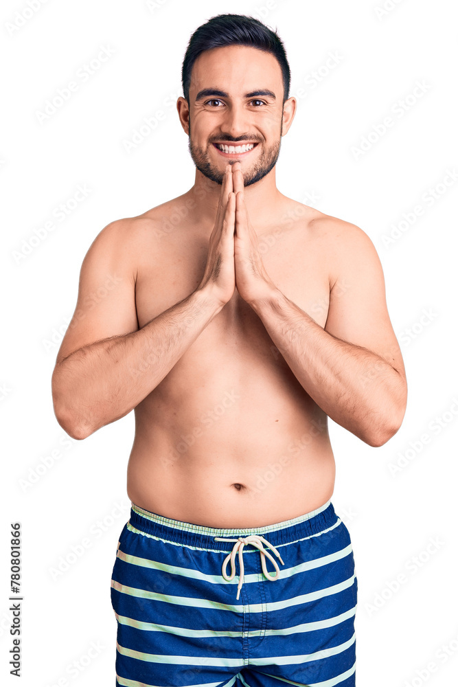 Young handsome man wearing swimwear praying with hands together asking for forgiveness smiling confident.