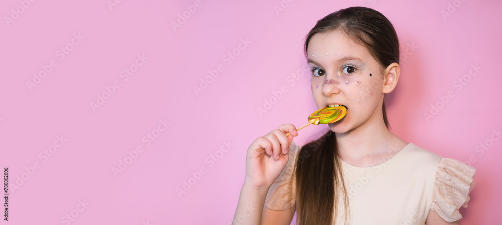 Banner. Portrait of happy smiling little girl with lollipop. Sugar for children. Little sweet tooth on pink background. Girl with bright makeup. Glittery glitter on face. Banner. Portrait of happy smiling little girl with lollipop. Sugar for children. Little sweet tooth on pink background. Girl with bright makeup. Glittery glitter on face.
