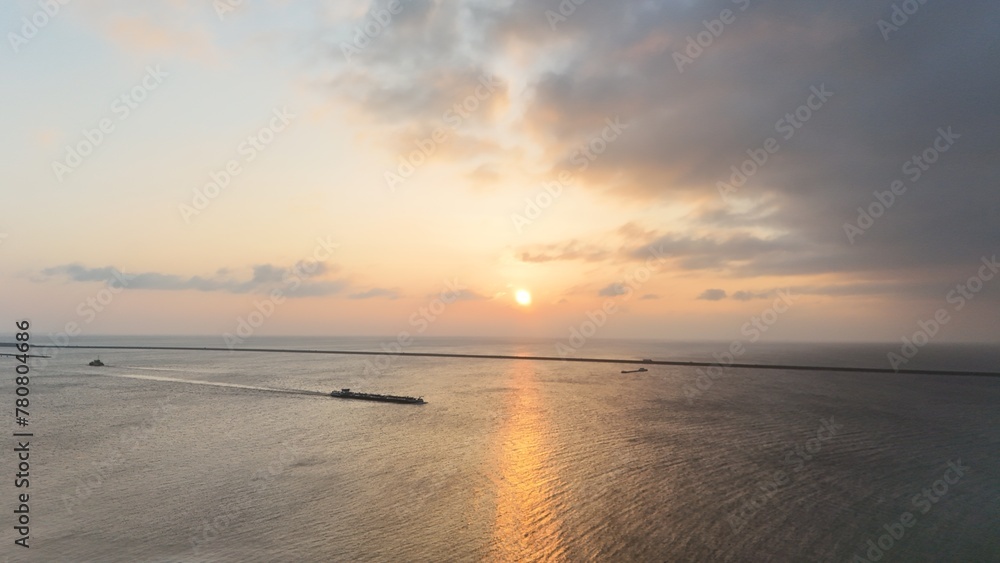 Serene sunset over calm ocean with clouds scattered in the sky, featuring gentle waves and a distant boat, ideal for backgrounds or nature themes.