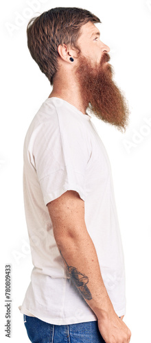 Handsome young red head man with long beard wearing casual white tshirt looking to side, relax profile pose with natural face with confident smile.