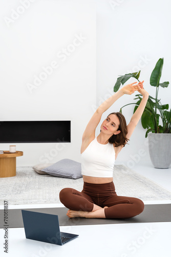 Young woman doing exercise at home and watching online classes using laptop. Copy space.