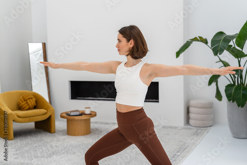 Young woman doing yoga warrior pose during yoga practice at home. Copy space.