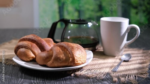 Cornetti sul piatto bianco in primo piano, tazza bianca e teglia con caffè tovaglietta di stoffa e cucchiaino photo
