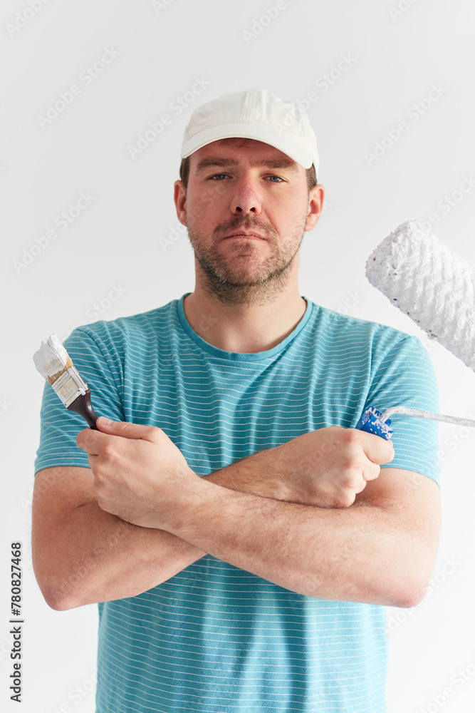 Smiling man holding a brush and a roller in front of him Smiling man holding a brush and a roller in front of him