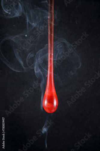 Gota de vidro vermelho semi transparente em fundo preto. Fotografia em close up de uma peça similar a um líquido de alta viscosidade pingando. photo