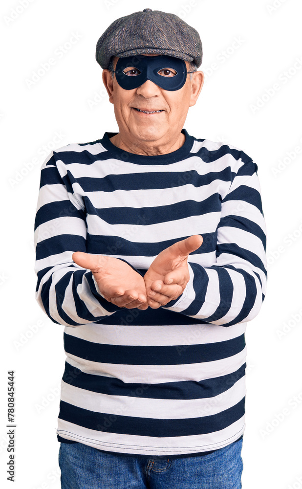 Senior handsome man wearing burglar mask and t-shirt smiling with hands palms together receiving or giving gesture. hold and protection Senior handsome man wearing burglar mask and t-shirt smiling with hands palms together receiving or giving gesture. hold and protection