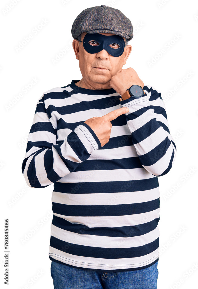 Fototapeta premium Senior handsome man wearing burglar mask and t-shirt in hurry pointing to watch time, impatience, looking at the camera with relaxed expression