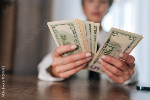 Selective focus of female counting money cash dollars bills one, five, ten, twenty and one hundred dollar banknote sitting at table. Concept of financial accounting budget planning, revenue, wealth photo