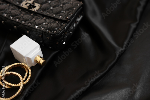 Leather bag, bottle of perfume and golden bracelets on black fabric, closeup. Space for text