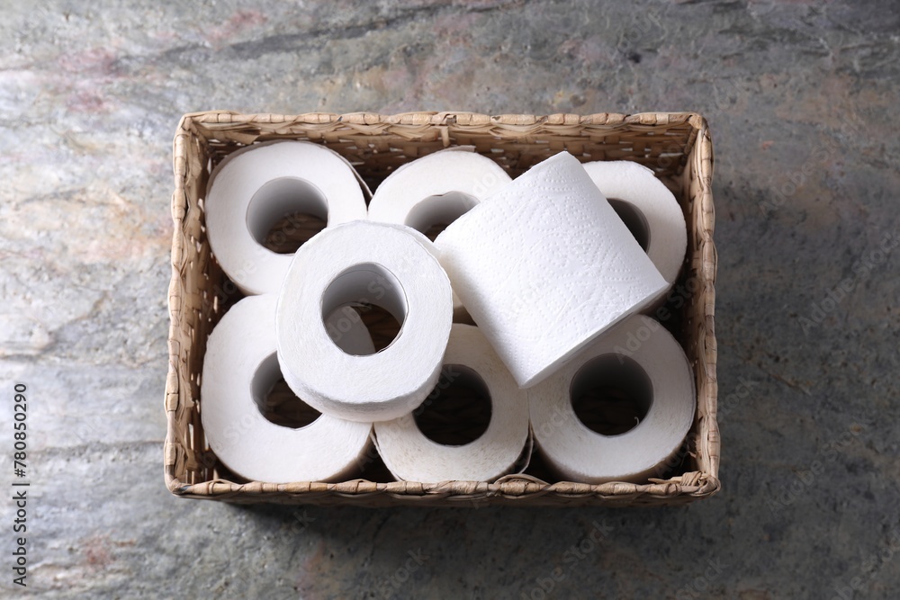 Fototapeta premium Toilet paper rolls in wicker basket on textured table, top view
