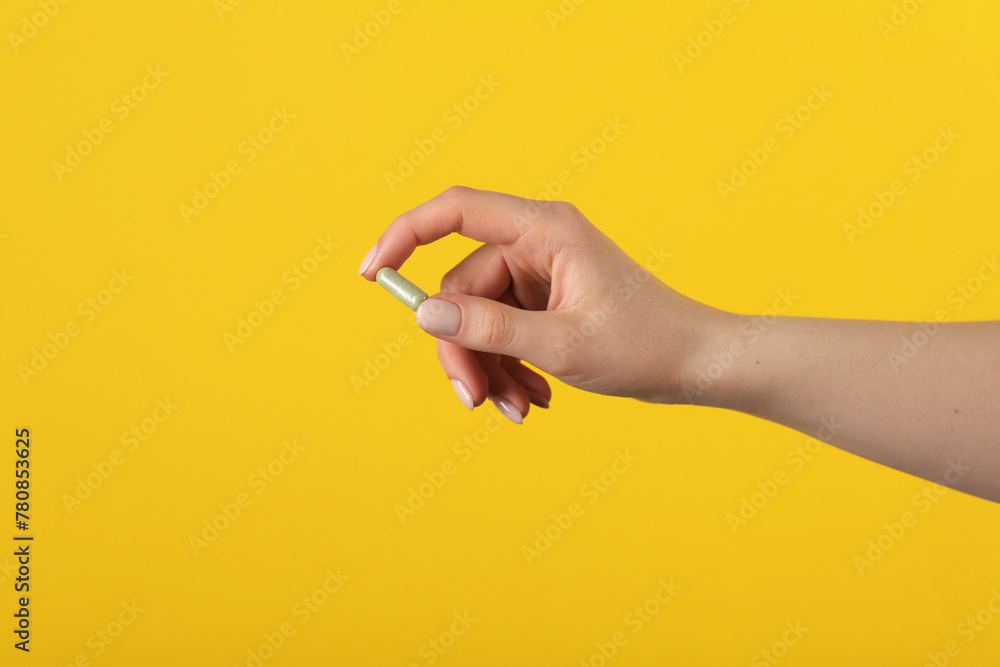 Woman holding vitamin pill on yellow background, closeup. Health supplement - obrazy, fototapety, plakaty 
