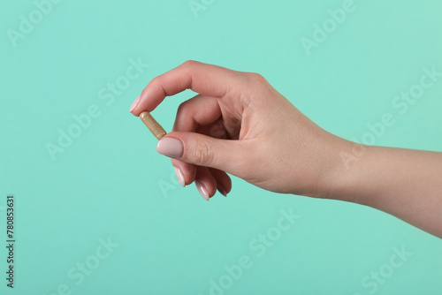 Woman holding vitamin capsule on turquoise background, closeup. Health supplement