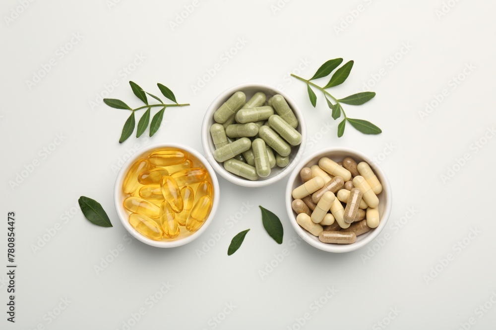 Different vitamin capsules in bowls and leaves on white background, flat lay Different vitamin capsules in bowls and leaves on white background, flat lay